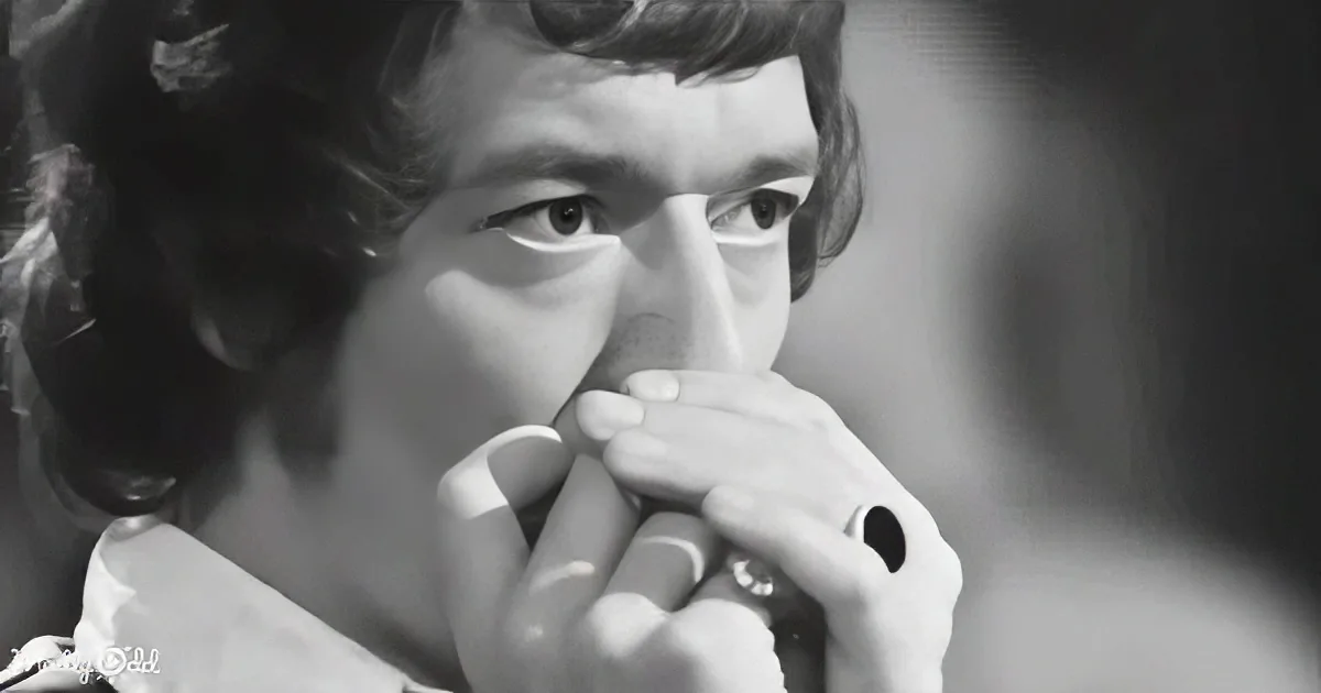 A person with curly hair and a white shirt is holding a harmonica close to their mouth.