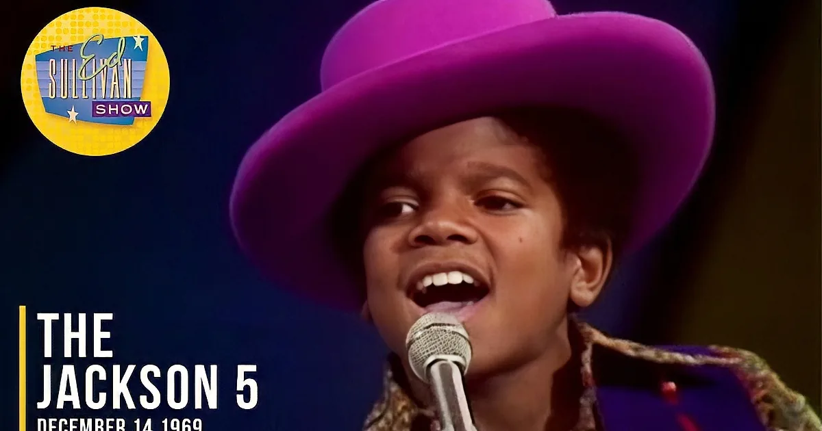 A child wearing a large purple hat sings into a microphone.