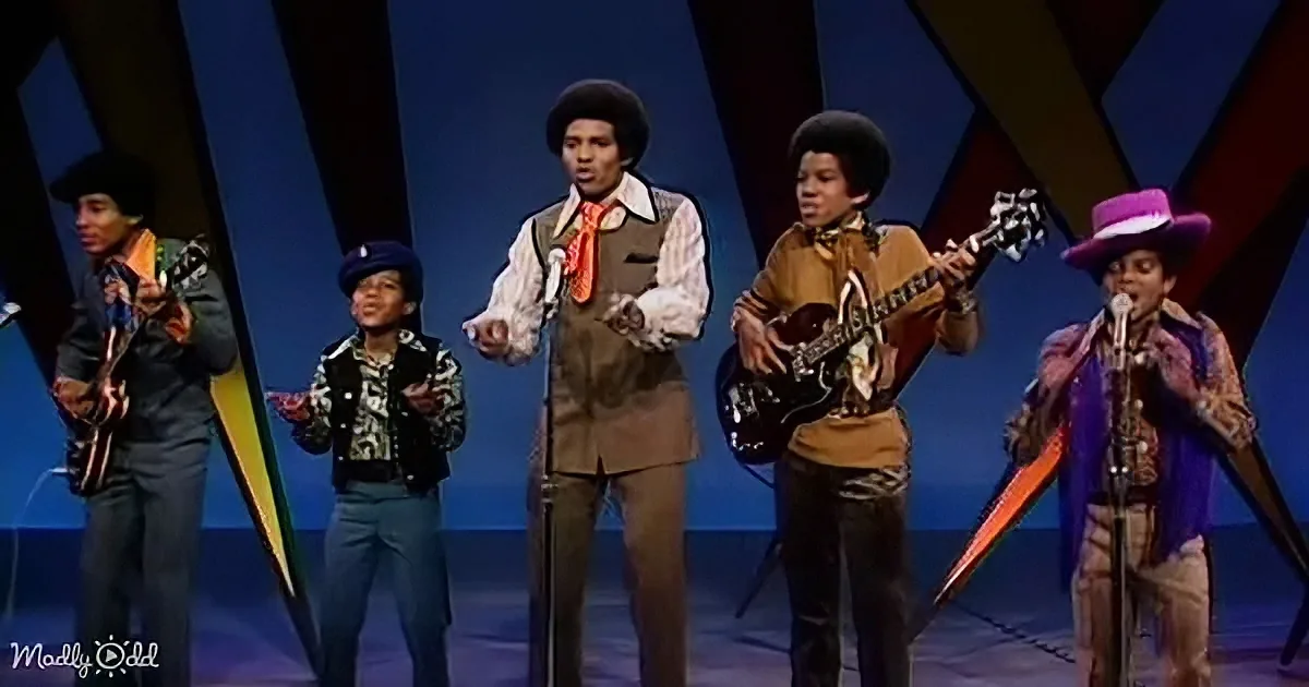 A group of five young musicians performing on stage, each with a unique outfit and instrument.