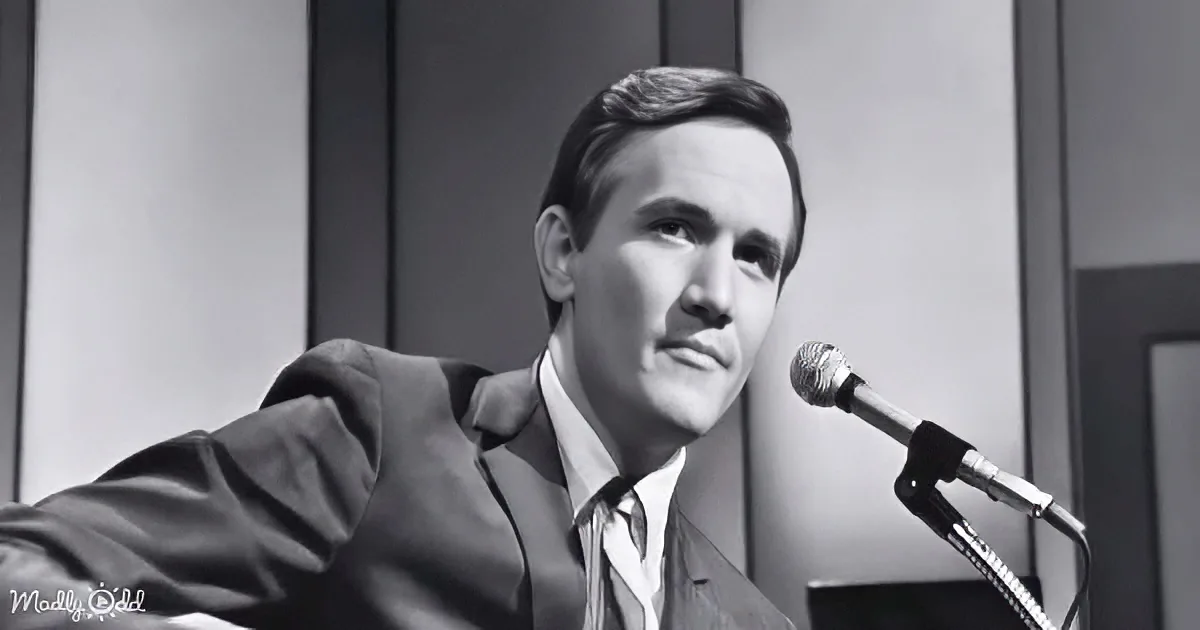 A man in a suit and tie is speaking into a microphone, appearing to be in a formal setting.
