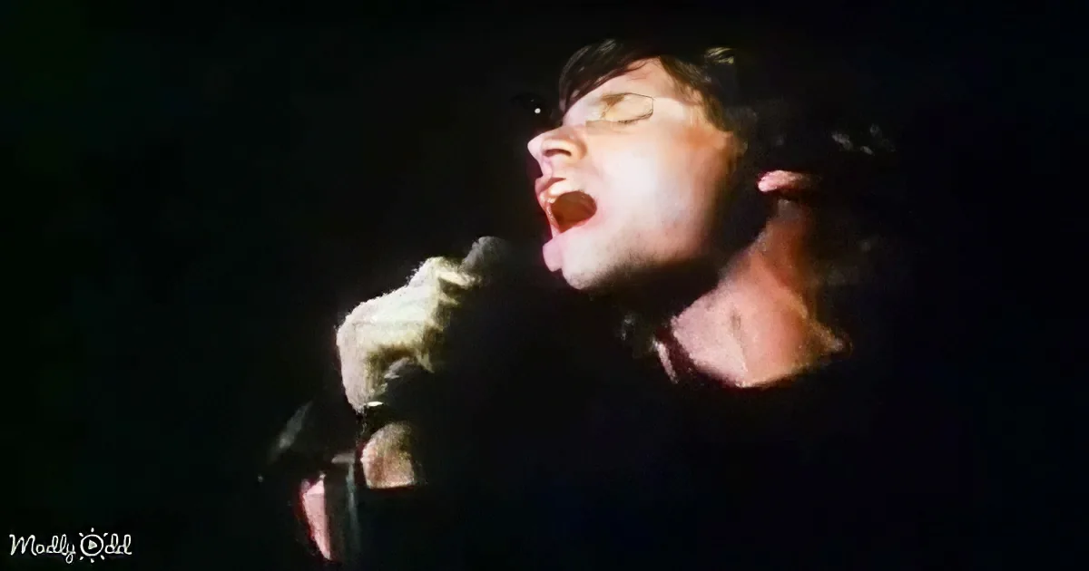 A person passionately sings into a microphone, illuminated against a dark background.