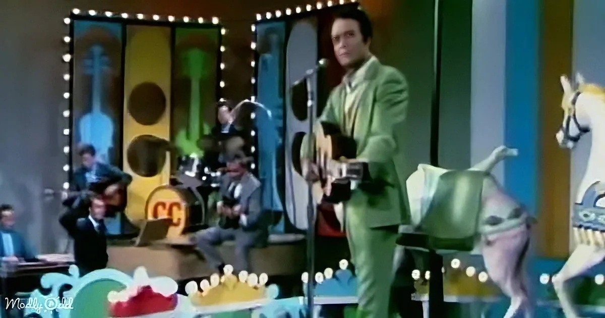 Elvis Presley in a green suit performs on stage with a band and colorful backdrop.