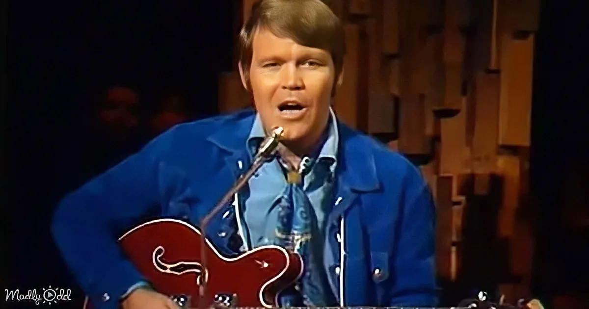 A man in a blue outfit sings into a microphone while holding a red guitar.