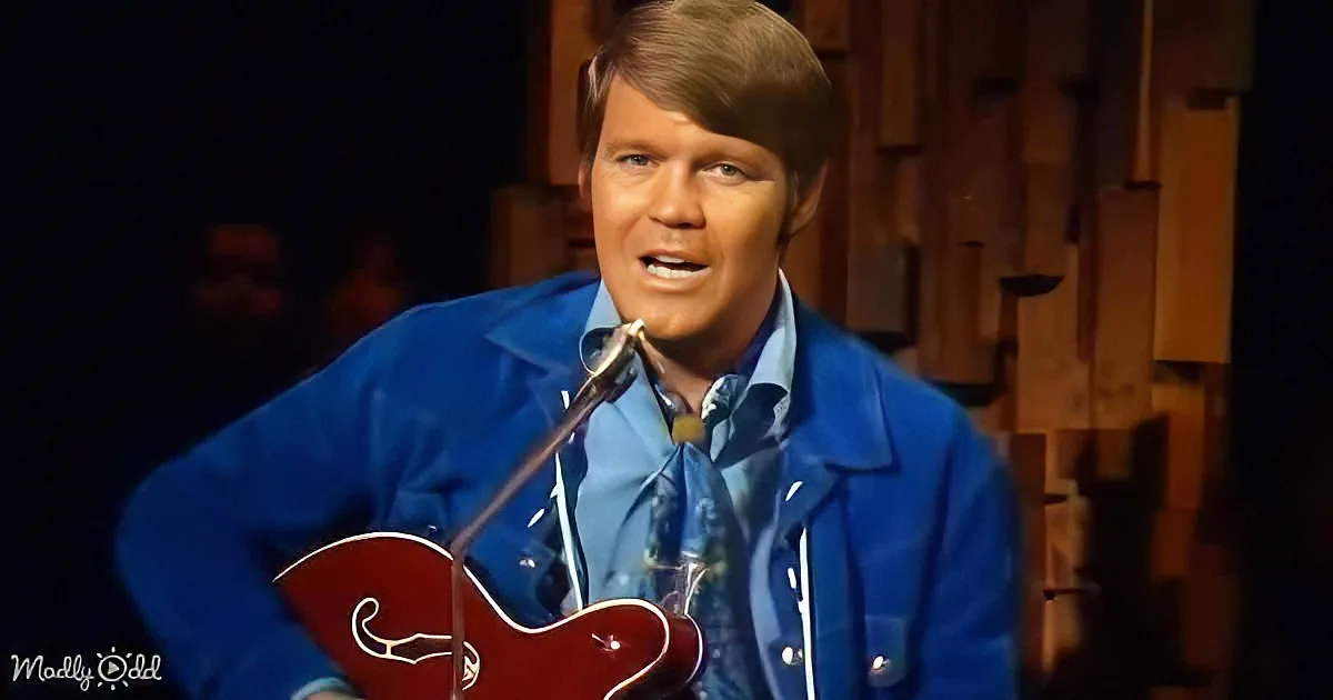 A man in a blue suit plays a red guitar on stage with a microphone.