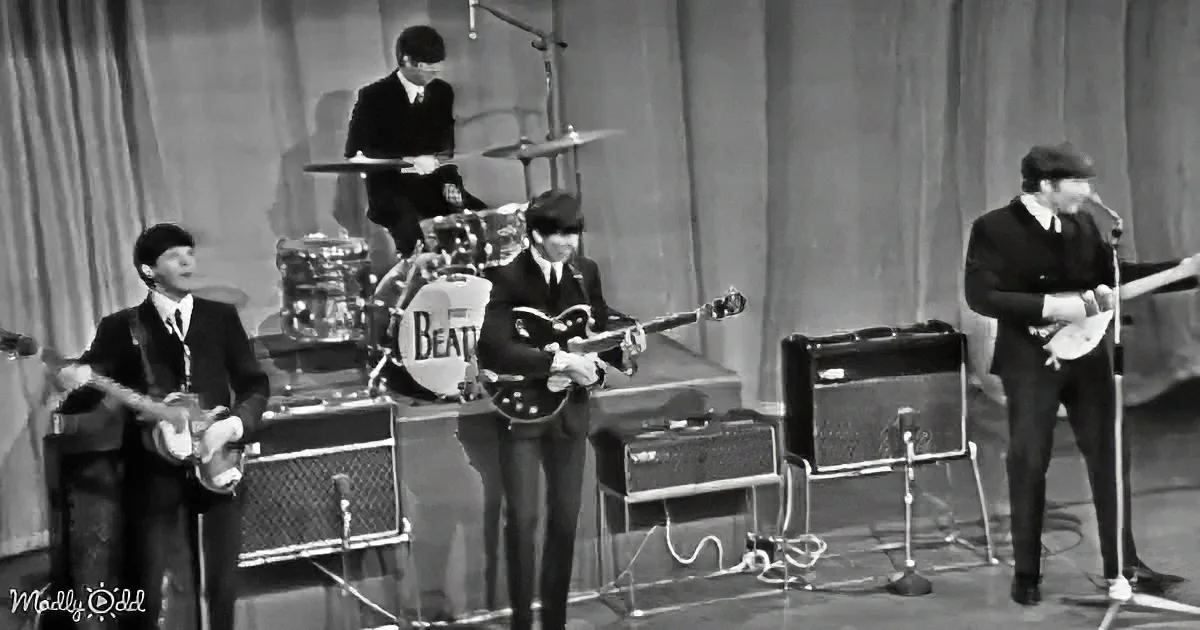The Beatles perform on stage, each member playing their instrument, dressed in suits and ties.