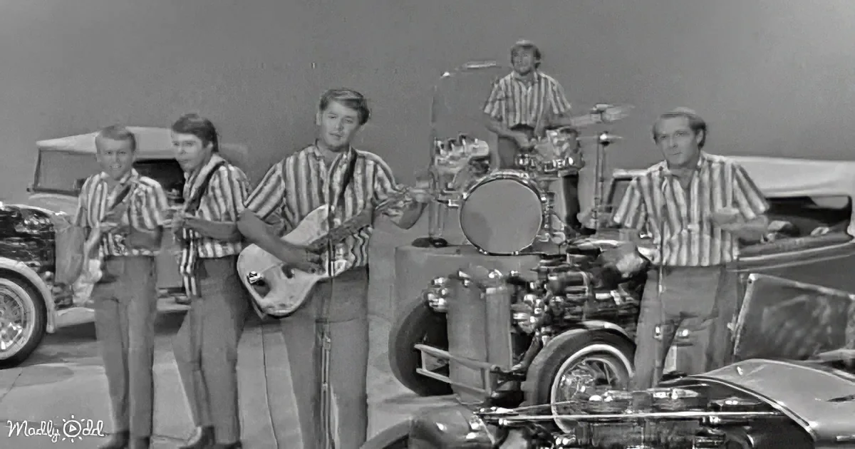 A band in striped shirts plays instruments in front of vintage cars, creating a retro vibe.