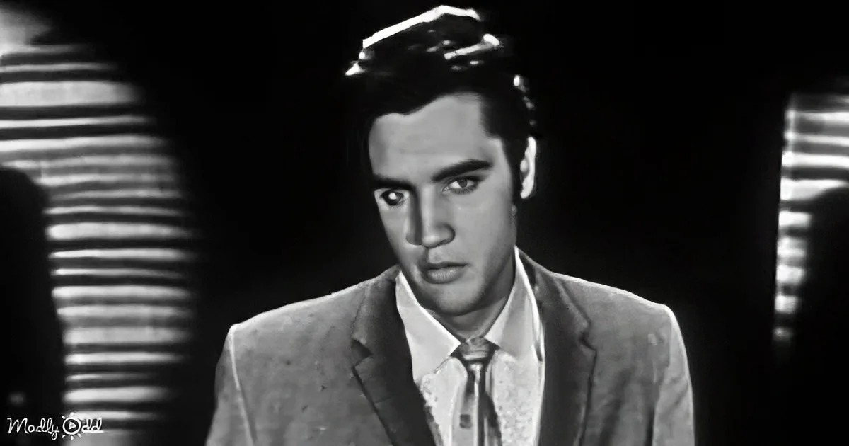 Elvis Presley in a suit and tie, looking serious, with a shadowy background.