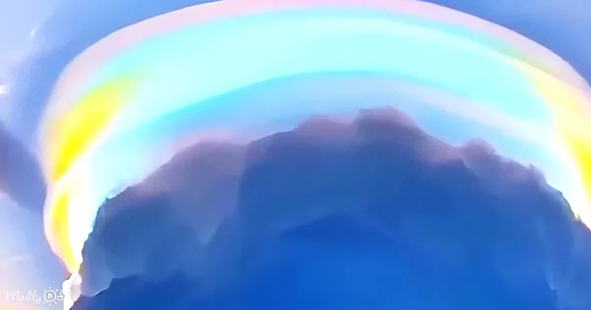 A vibrant rainbow arches over a dark, textured mountain peak against a bright blue sky.