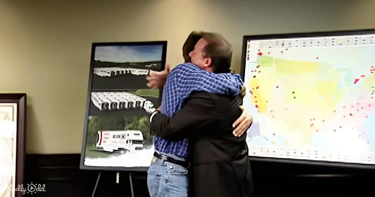 Two men embrace in front of a map and a display showing images of a road and a truck.