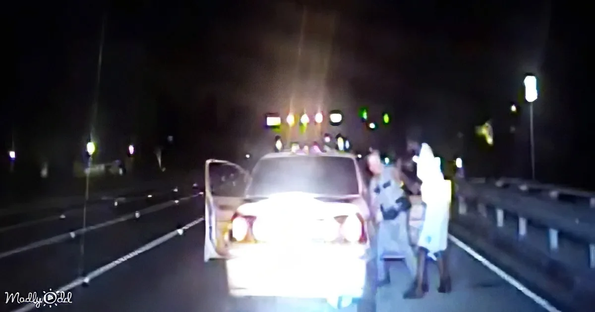 A car is stopped at a toll booth with two people standing beside it at night.