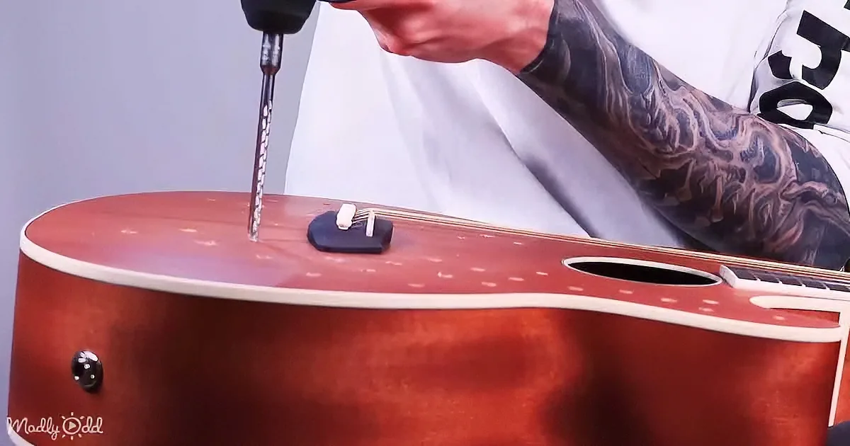 A tattooed person drills into a guitar's sound hole.