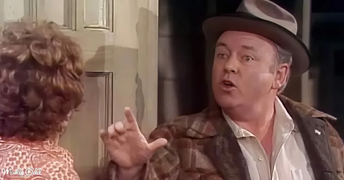 A man in a hat and plaid jacket gestures while speaking to a woman with curly hair.