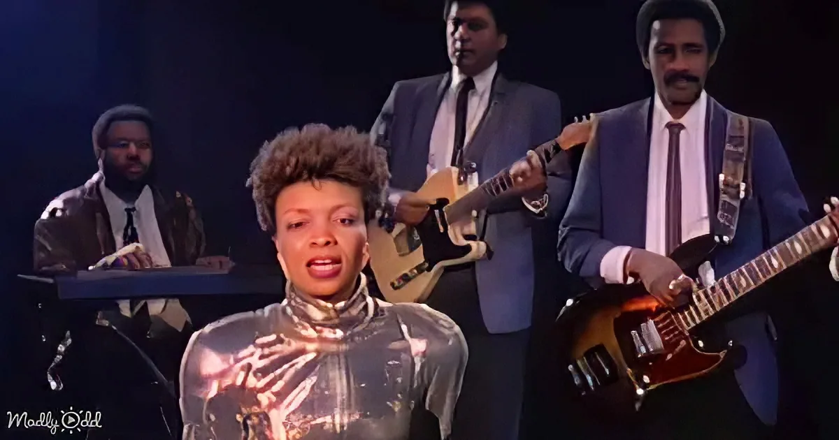 A woman in a reflective outfit sings, surrounded by musicians in suits playing instruments.