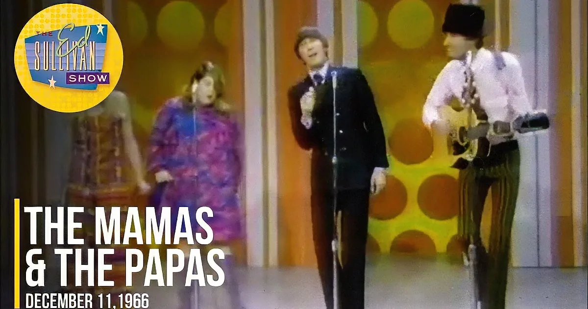 A woman in a colorful dress sings into a microphone, joined by a man in a hat and another in a suit, both also singing.