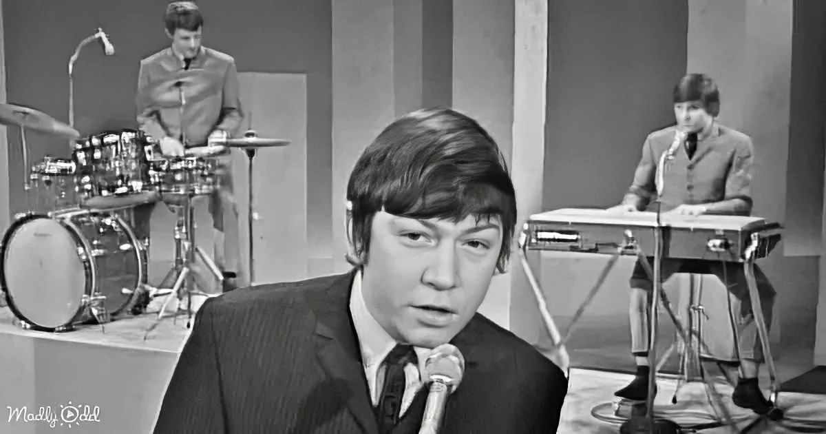 A man in a suit sings into a microphone, with a band playing in the background.
