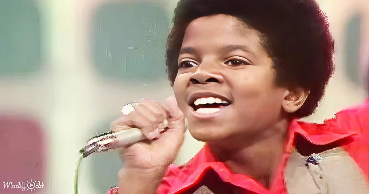 A young person in a red shirt holds a microphone, smiling with a joyful expression.