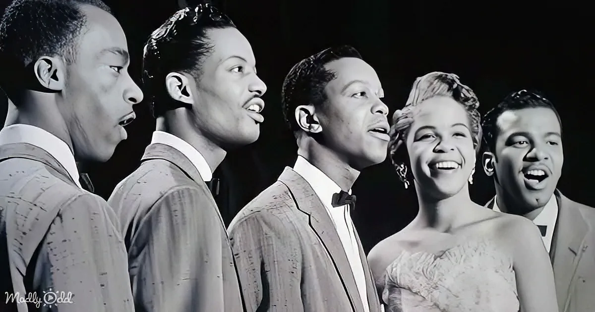 A group of five individuals, dressed formally, are singing together in a black-and-white image.