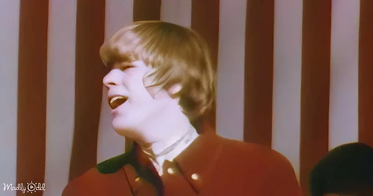 A person with short, light brown hair wearing a red and green outfit is singing.