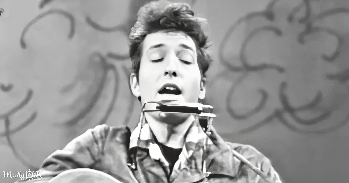 A person with closed eyes and a harmonica in their mouth, wearing a jacket, against a blurred background.