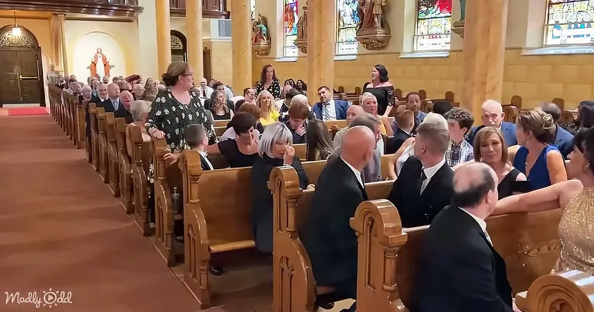 A woman in a polka-dot dress stands in a church aisle, surrounded by seated guests in formal attire.