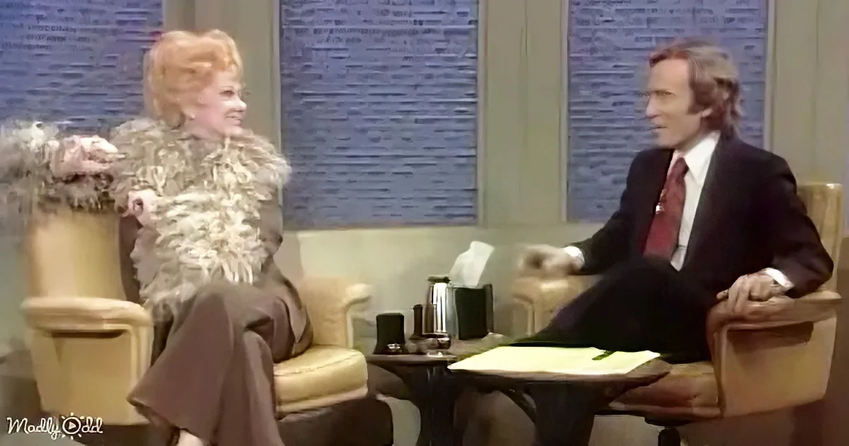 A woman in a fur coat sits on a chair, facing a man in a suit seated across from her in a therapy room setting.