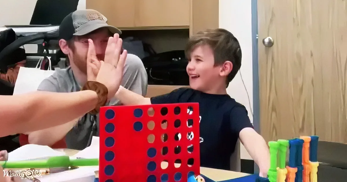 A boy in a black shirt gives a high-five to someone off-screen while playing a game with a red cube.