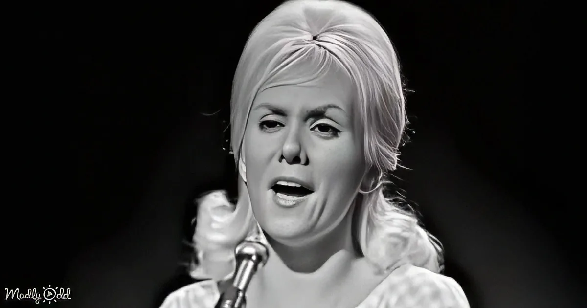 A woman with blonde hair in a bun sings into a microphone, captured in a black-and-white image.