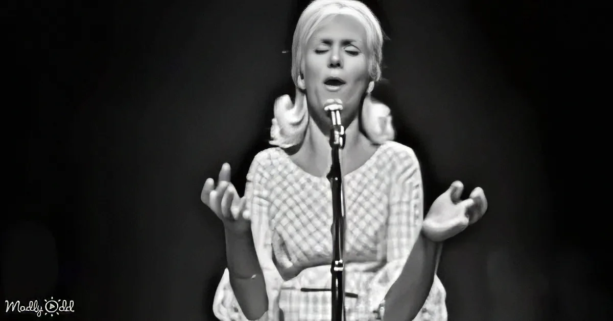 A woman in a checkered dress sings passionately into a microphone on stage.