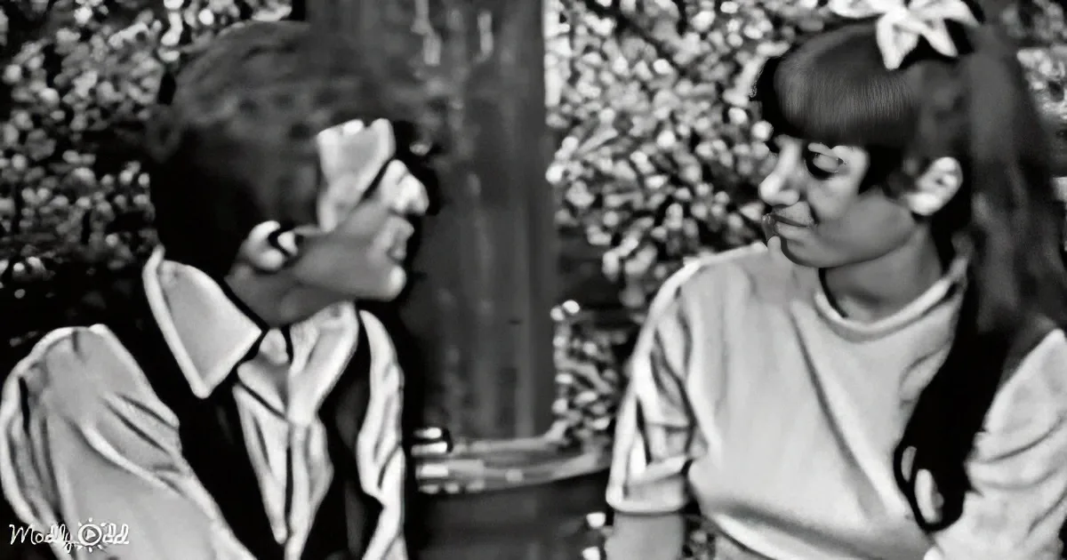 A man in a suit and tie leans forward, seemingly whispering to a woman with a ponytail and a white bow.