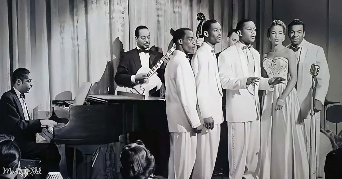 A jazz ensemble performs on stage, with a pianist, mandolinist, and a quartet of singers in white suits.