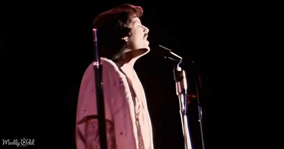 A person in a pink coat and beret sings passionately into a microphone on stage.