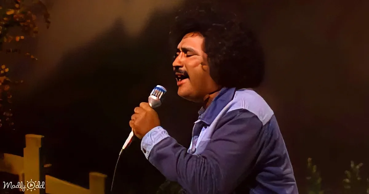 A man with an afro holds a microphone, singing passionately in a dimly lit setting.