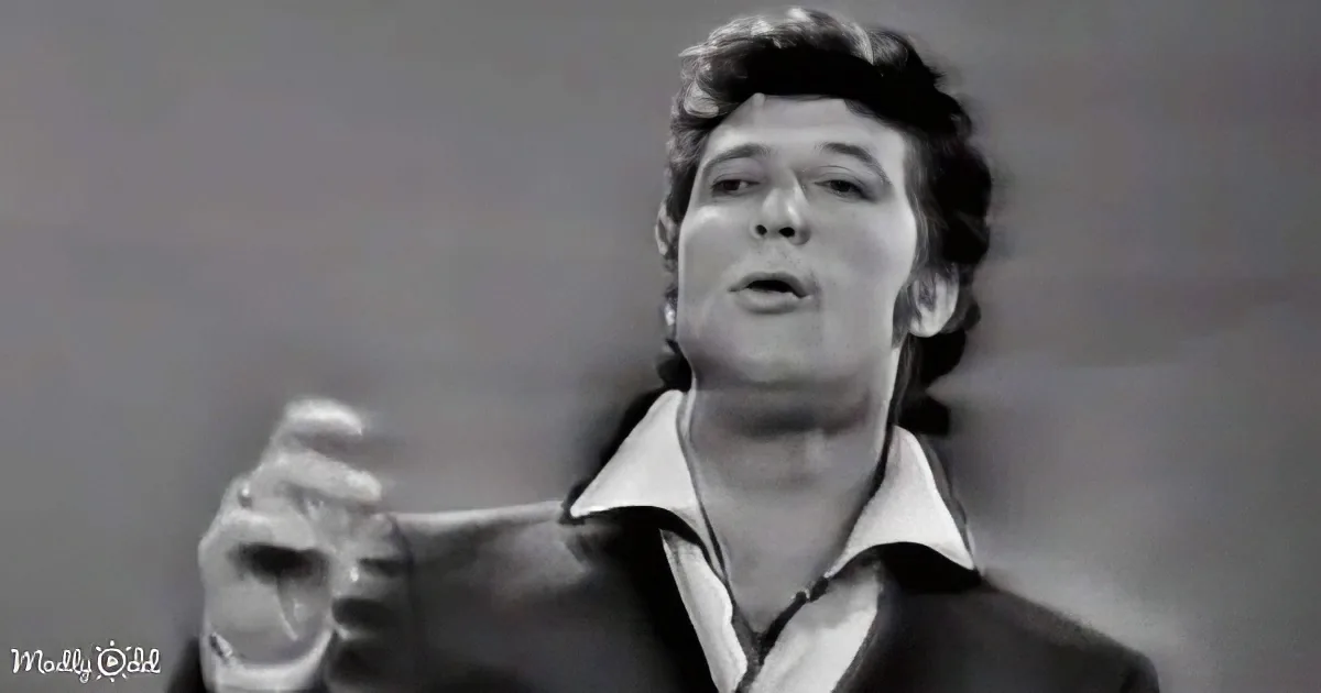 A man in a leather jacket and open shirt is singing passionately with his eyes closed.
