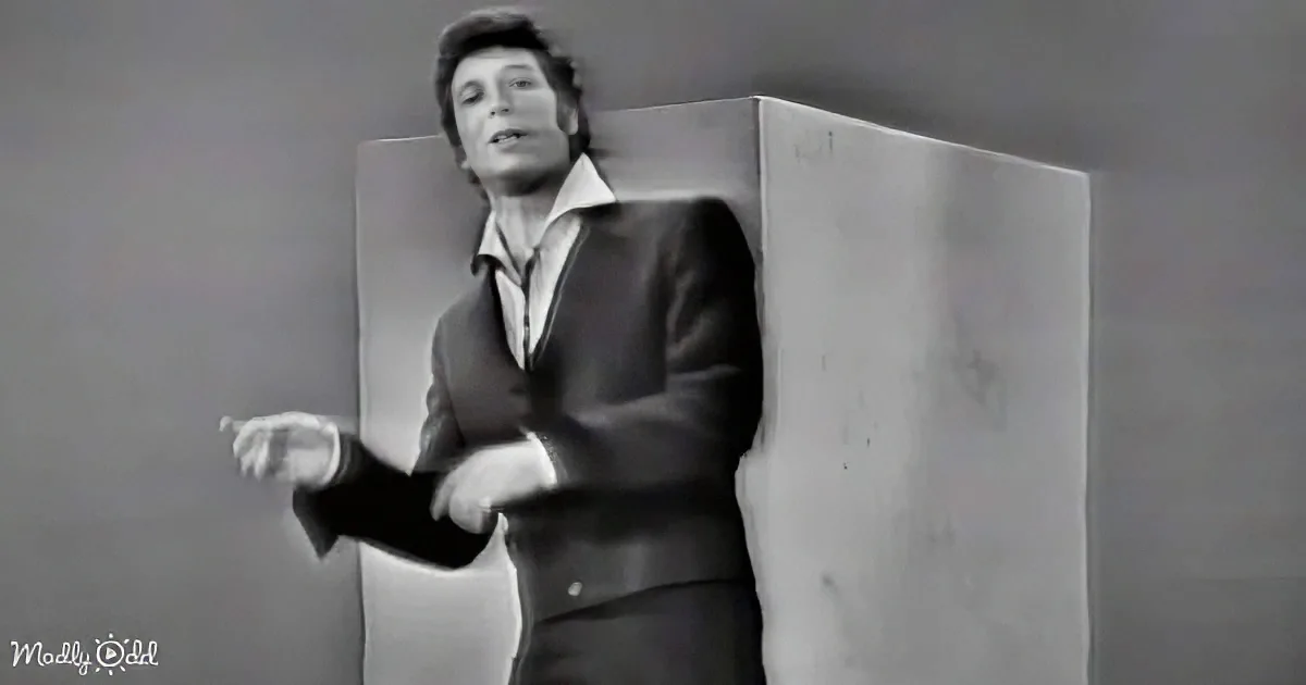 A person in a suit stands behind a large, rectangular object, appearing to be in motion or speaking.