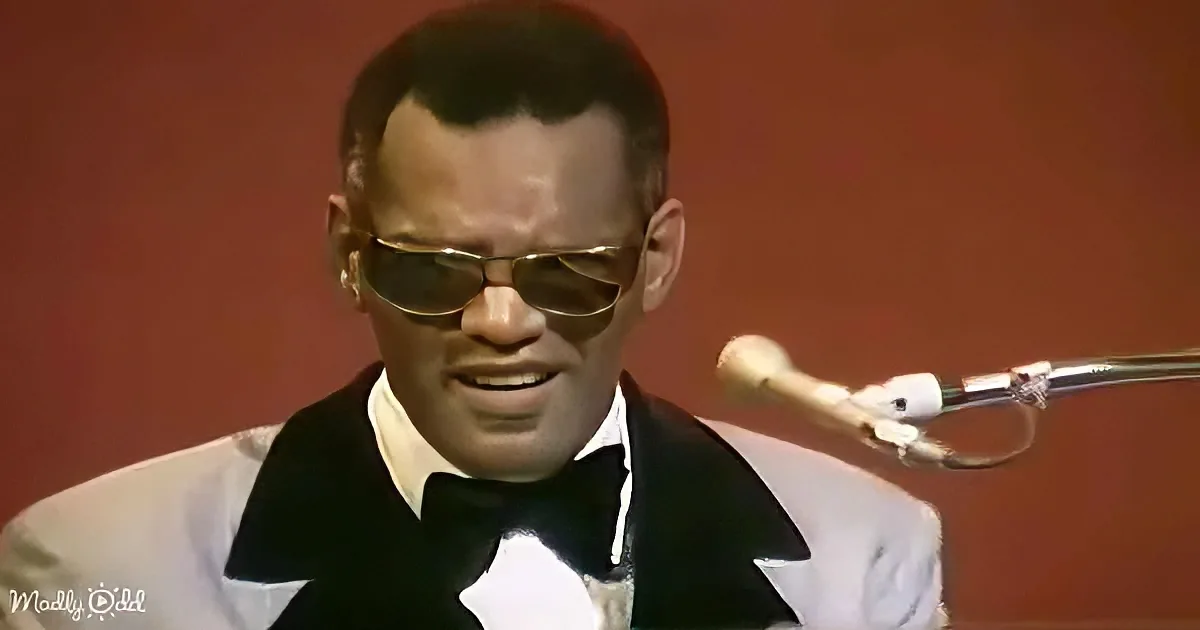 A man in a tuxedo and sunglasses sings into a microphone against a red background.