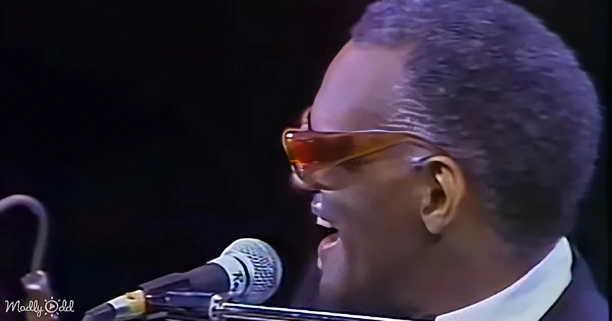A man wearing sunglasses sings into a microphone, wearing a white shirt and dark suit.