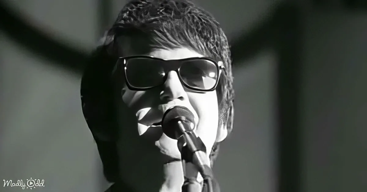 A person wearing sunglasses sings into a microphone, captured in a close-up black-and-white shot.