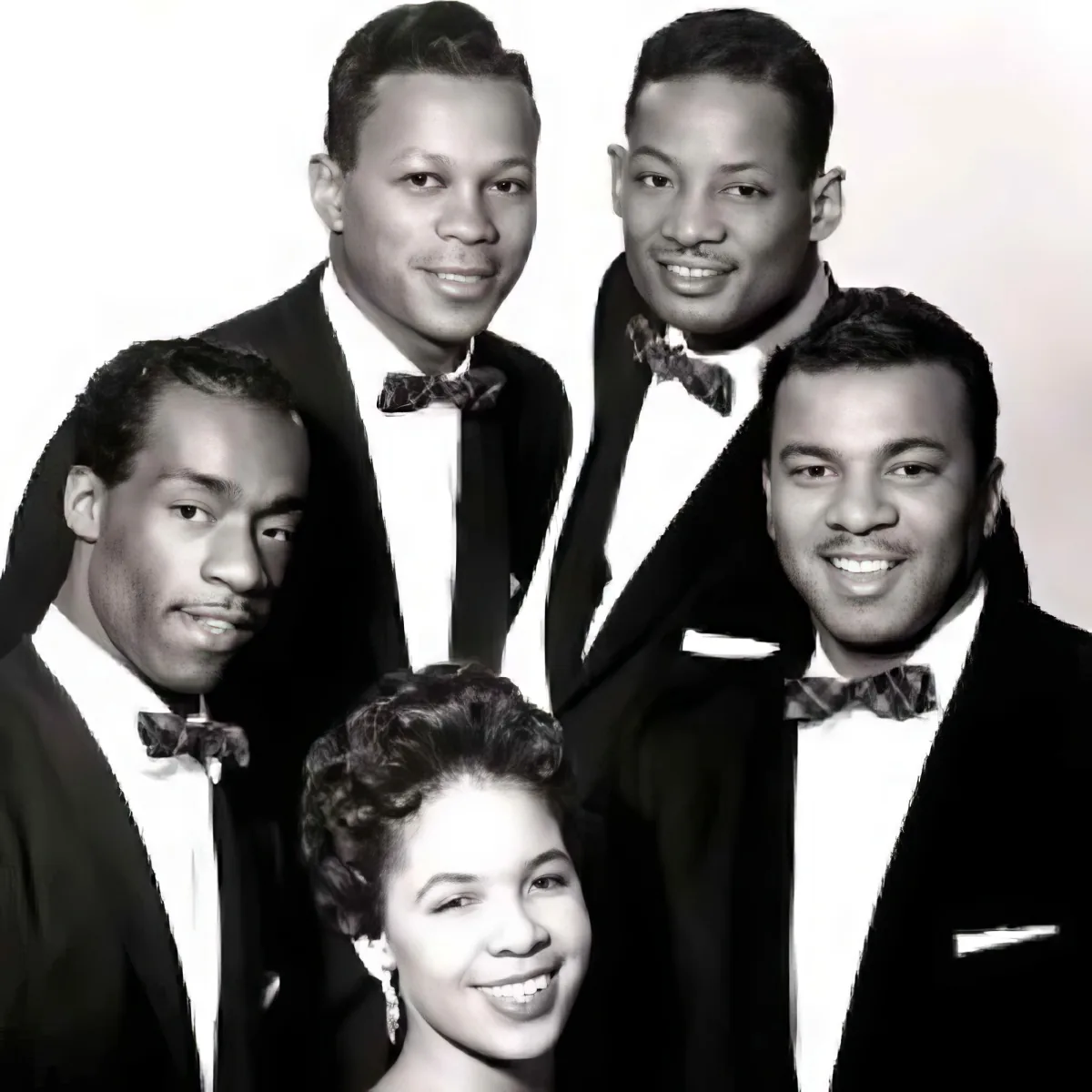 A group of five individuals, dressed in formal attire, pose together in a black-and-white photograph.