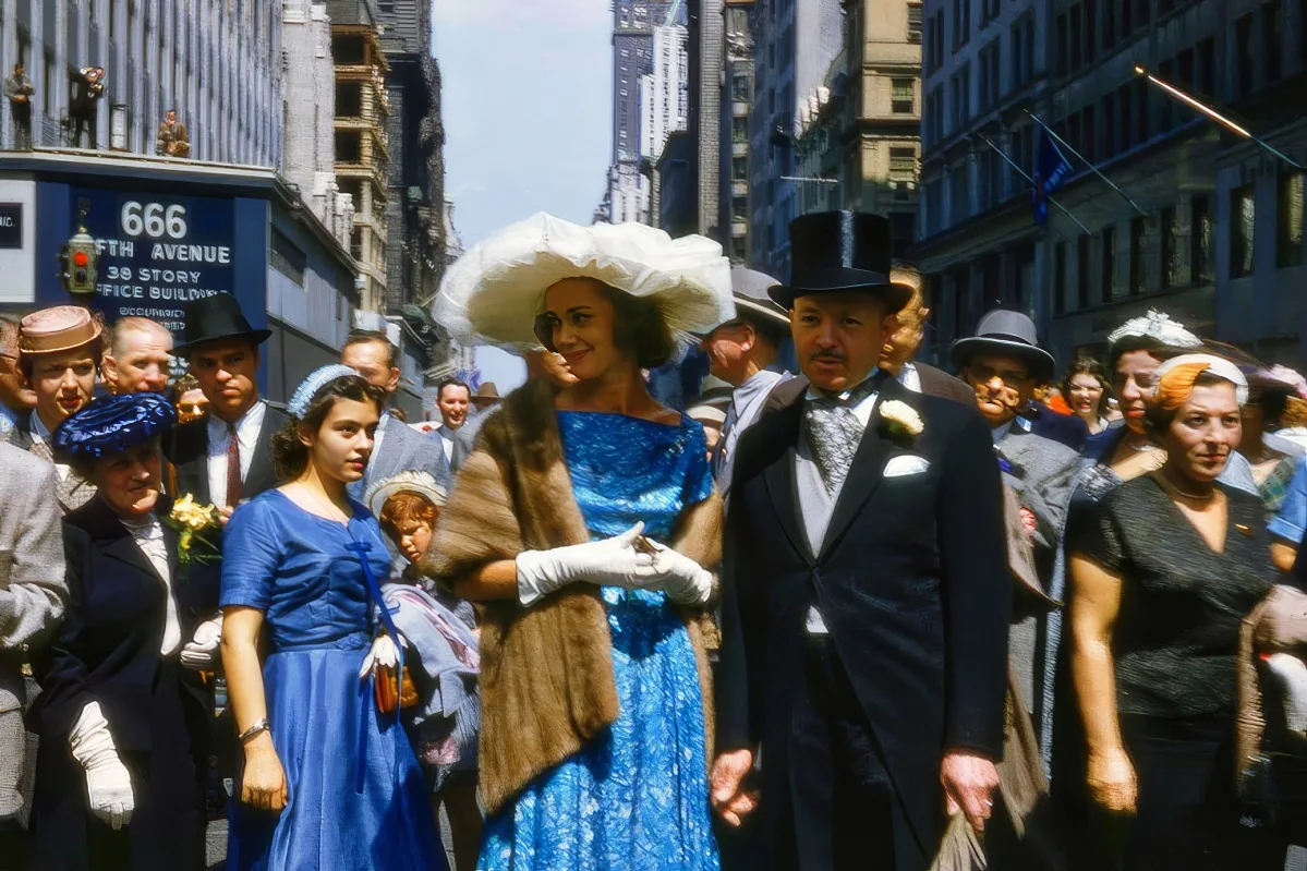 A woman in a blue dress and large white hat stands among a crowd in a bustling city street.