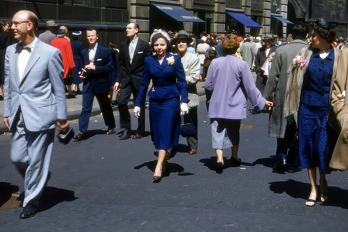 A woman in a blue suit walks confidently down a busy street, surrounded by other pedestrians in formal attire.