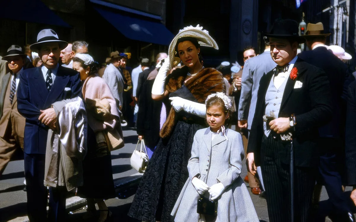 A woman in a fur coat and hat walks with a young girl in a light coat and gloves on a busy street.