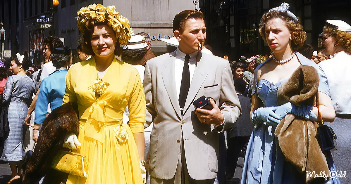 A woman in a yellow dress with a floral crown walks alongside a man in a suit and a woman in a blue dress with a fur stole.
