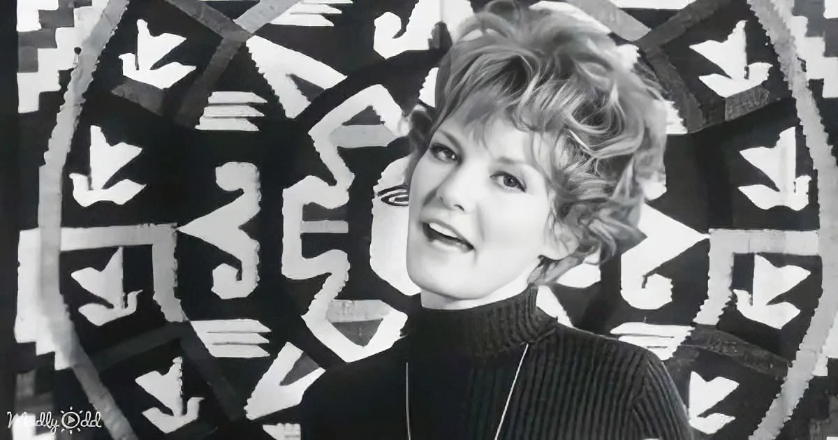 A woman with short, curly hair wearing a turtleneck stands in front of a black and white abstract background.