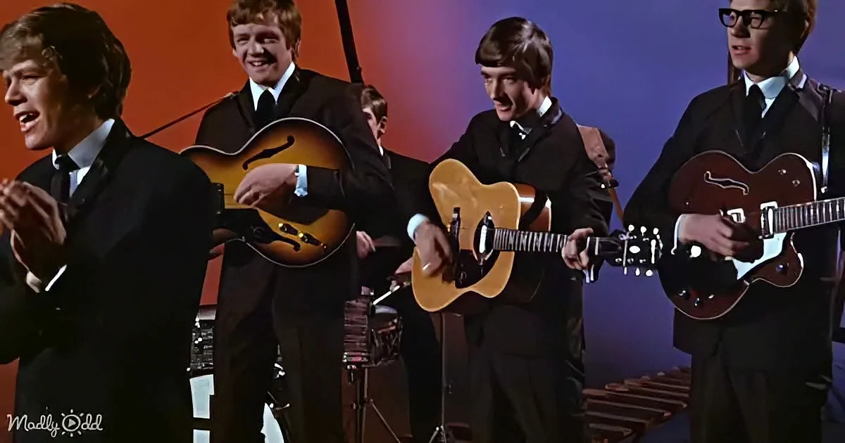 A group of musicians in suits play guitars and sing on stage, with a vibrant background.
