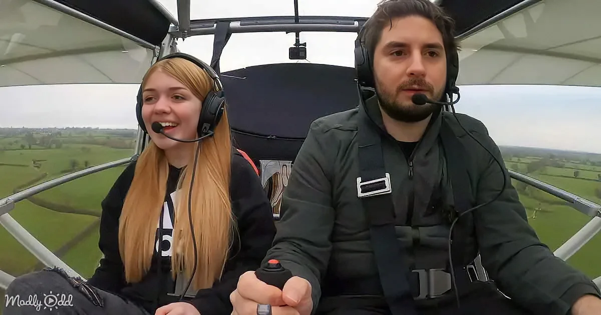 Two individuals in a small aircraft, both wearing headsets, with a scenic landscape visible through the open cockpit.