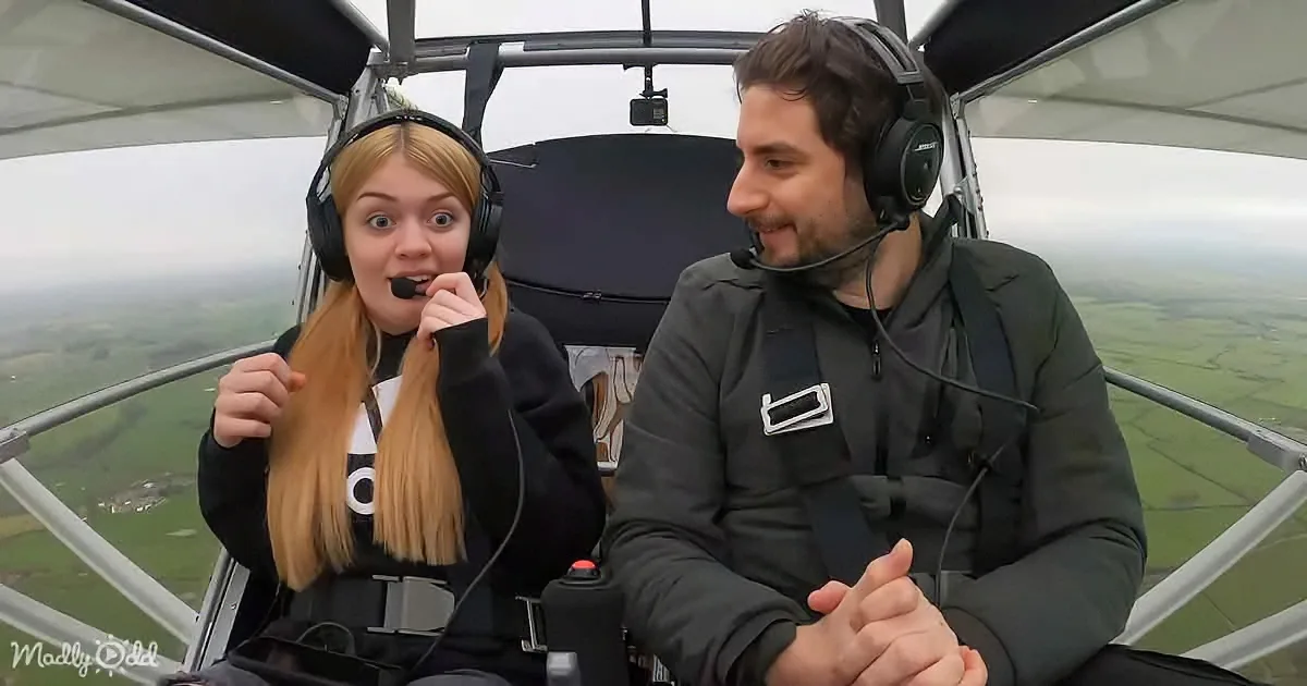 Two individuals wearing headsets are seated inside a small aircraft, with one appearing surprised and the other smiling.