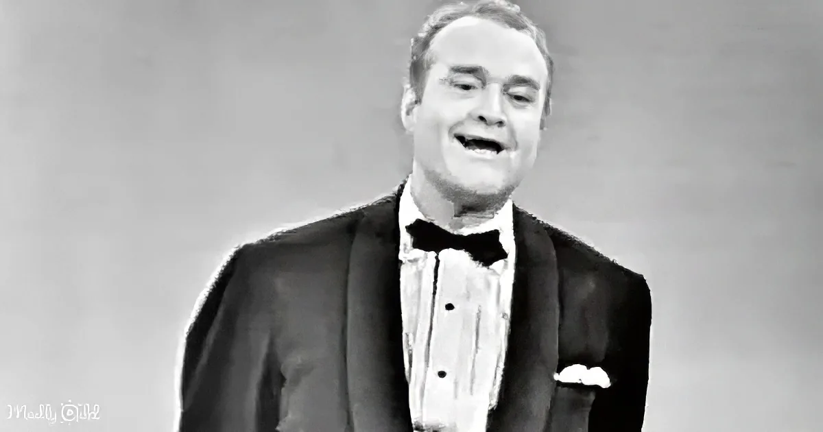 A man in a tuxedo and bow tie smiles widely, wearing a white shirt and black jacket.