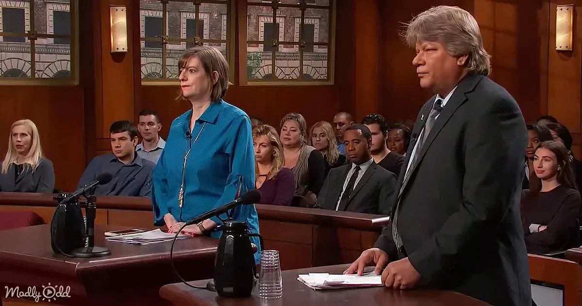 A woman in a blue blouse stands at a podium, facing a man in a suit in a courtroom setting.