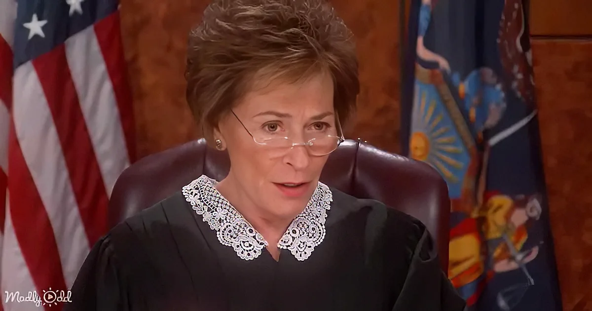 A woman in a judge's robe sits in a courtroom with an American flag and another flag behind her.