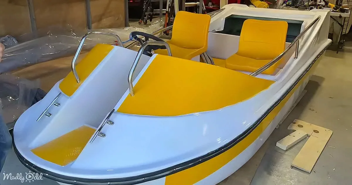 A yellow and white pedal boat with two seats and handlebars is displayed in a workshop setting.